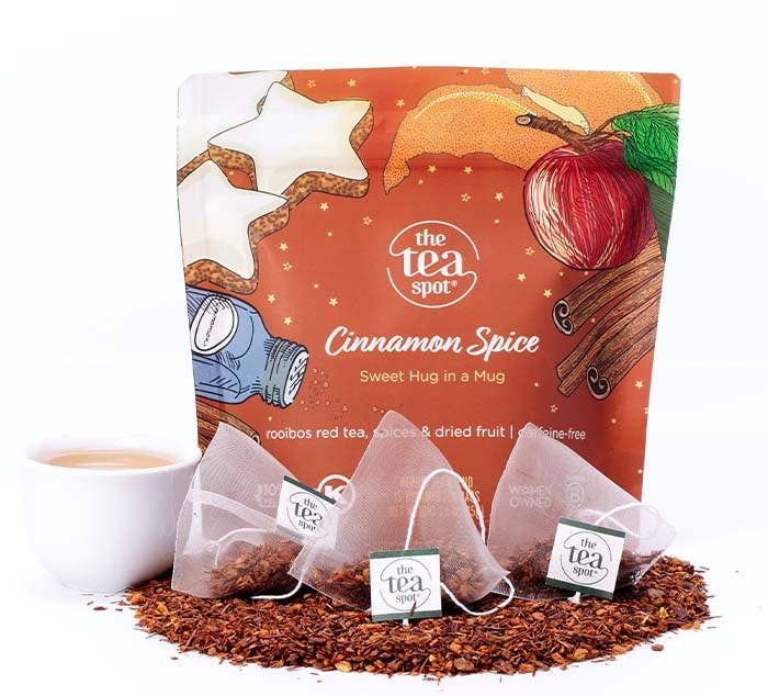 The Tea Spot Cinnamon Spice Rooibos Tea package containing 15 tea sachets, displayed with a cup of amber-colored tea, cinnamon sticks, and loose rooibos tea.