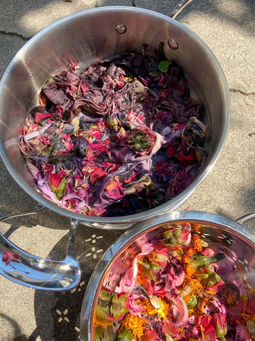 Two metal bowls filled with colorful dried flower petals on a concrete surface.