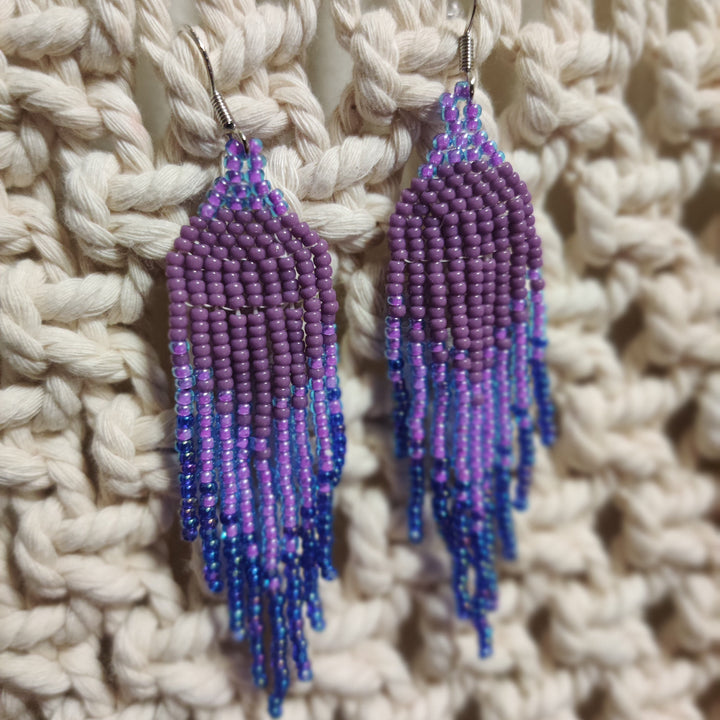 Purple and blue beaded earrings on a woven beige background