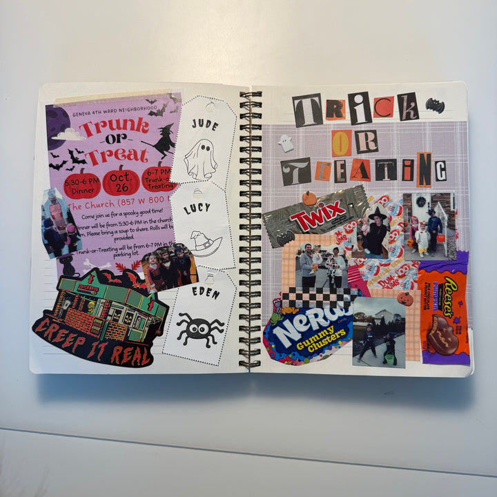 An open spiral notebook showing a Halloween-themed collage spread with stickers, cutout letters, ghost illustrations, candy graphics, and handwritten notes on a white surface.
