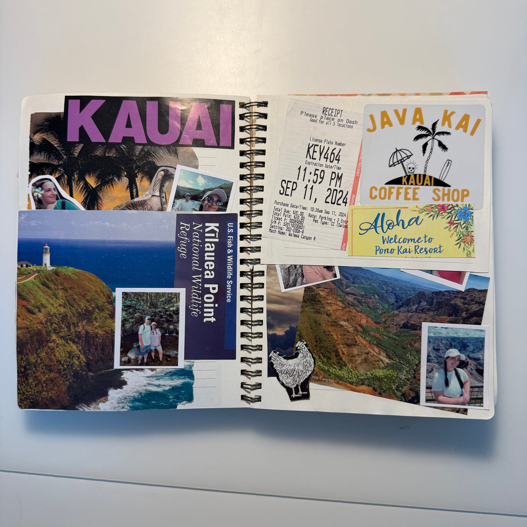 An open spiral-bound notebook or planner spread on a white surface, filled with travel-themed stickers and printed inserts including the word &