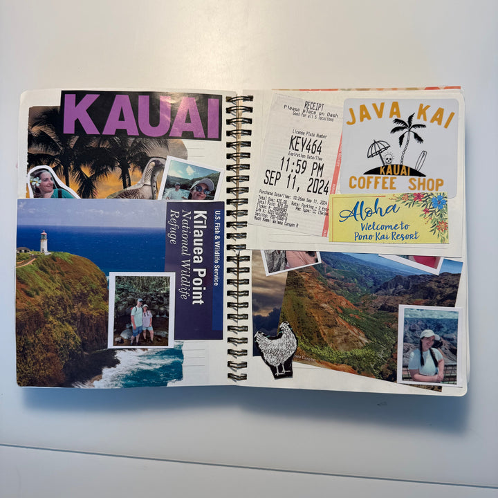 An open spiral-bound notebook or planner spread on a white surface, filled with travel-themed stickers and printed inserts including the word &