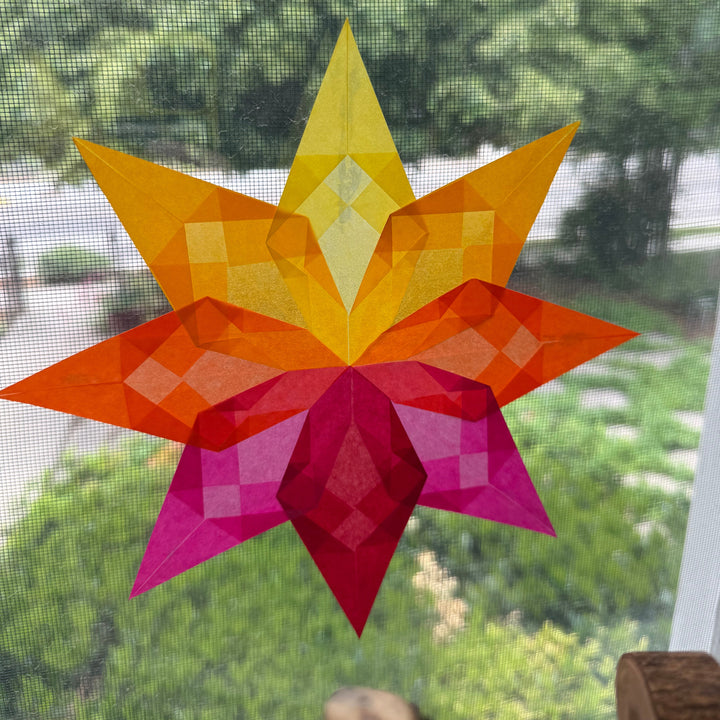 Geometric star-shaped decoration with orange and pink colors against a blurred green outdoor background.