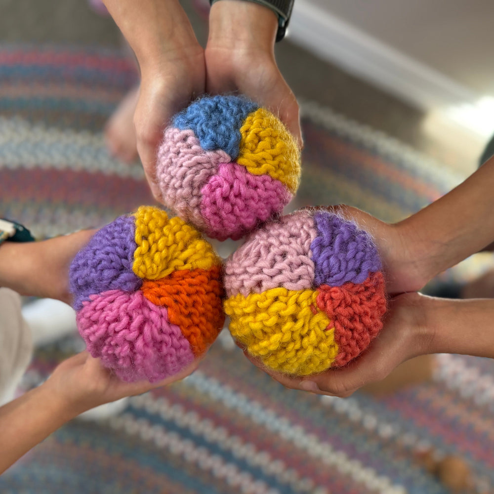 Three hands holding colorful Knit balls against a blurred indoor background