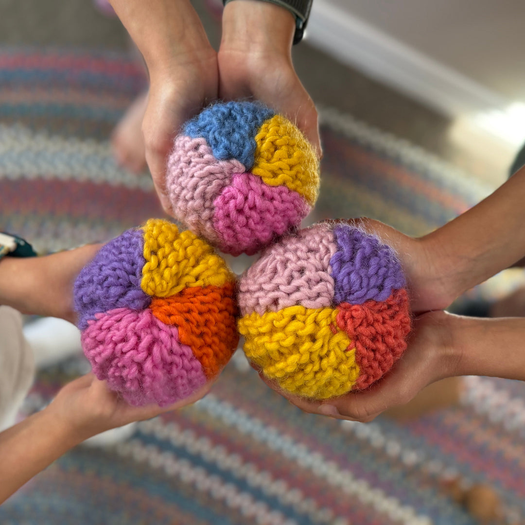 Three hands holding colorful Knit balls against a blurred indoor background