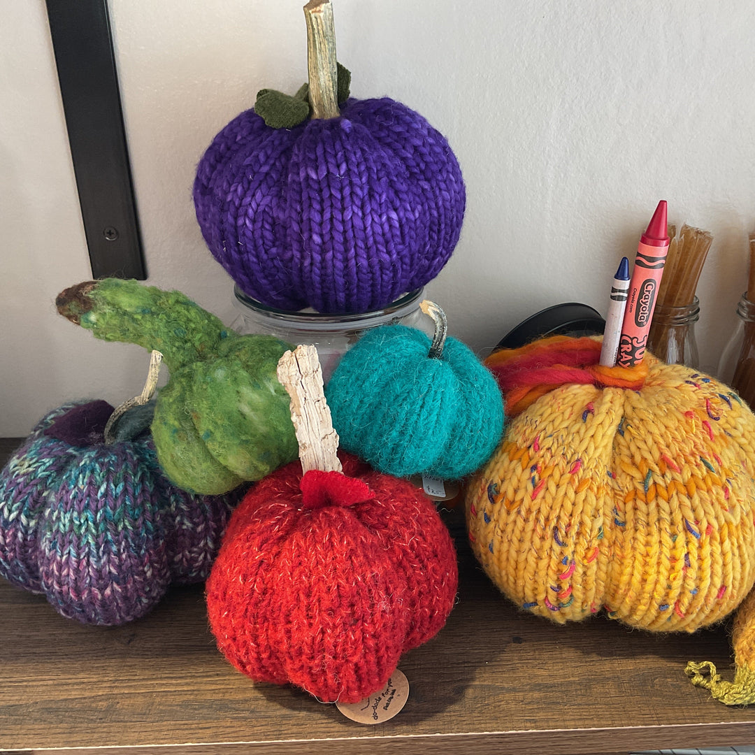Colorful knitted pumpkins on a shelf with crayons and other items.