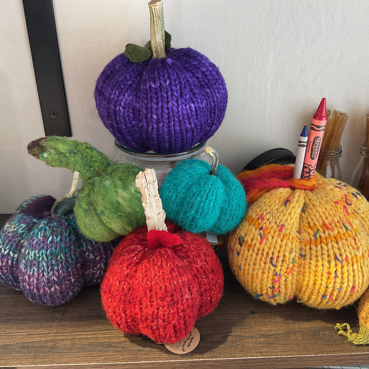 Colorful knitted pumpkins on a shelf with crayons and other items.