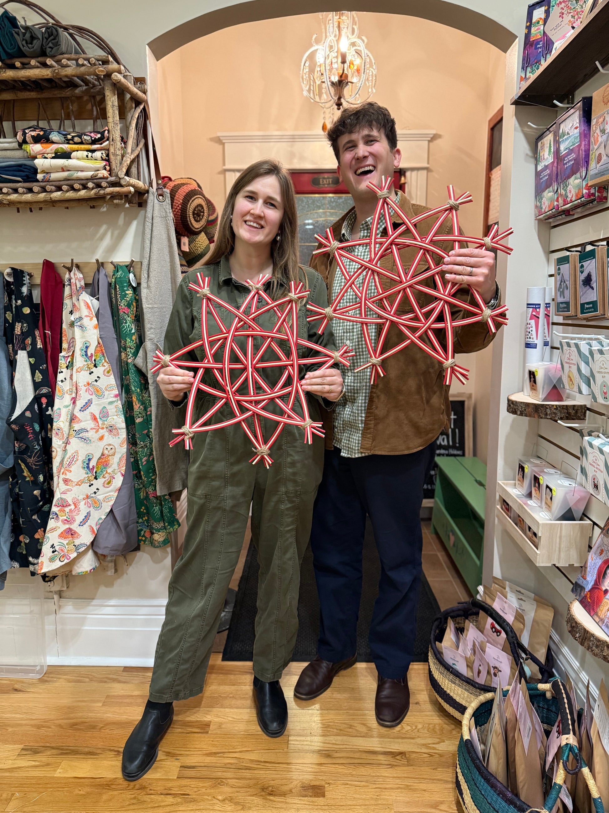 A man and a woman standing in a boutique shop holding red geometric woven star ornaments.