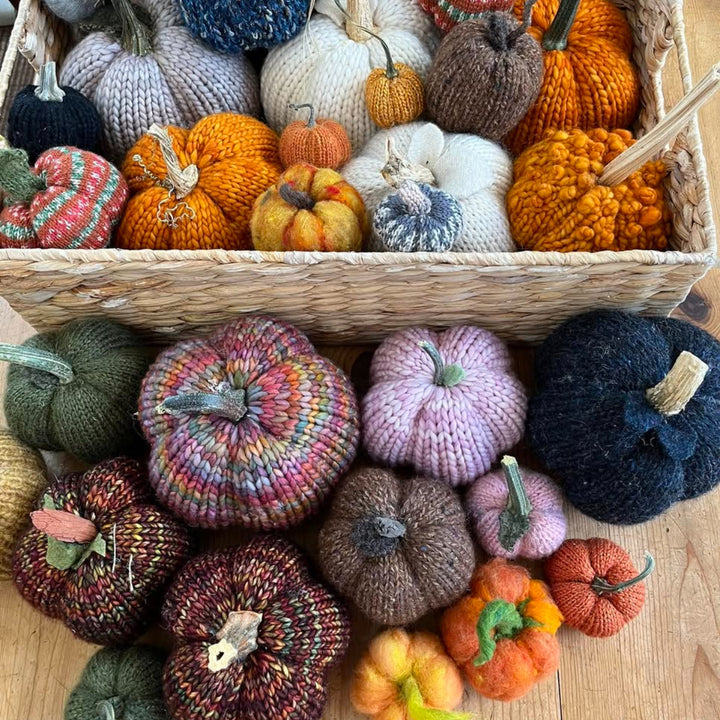 Basket filled with colorful knitted pumpkins on a wooden surface