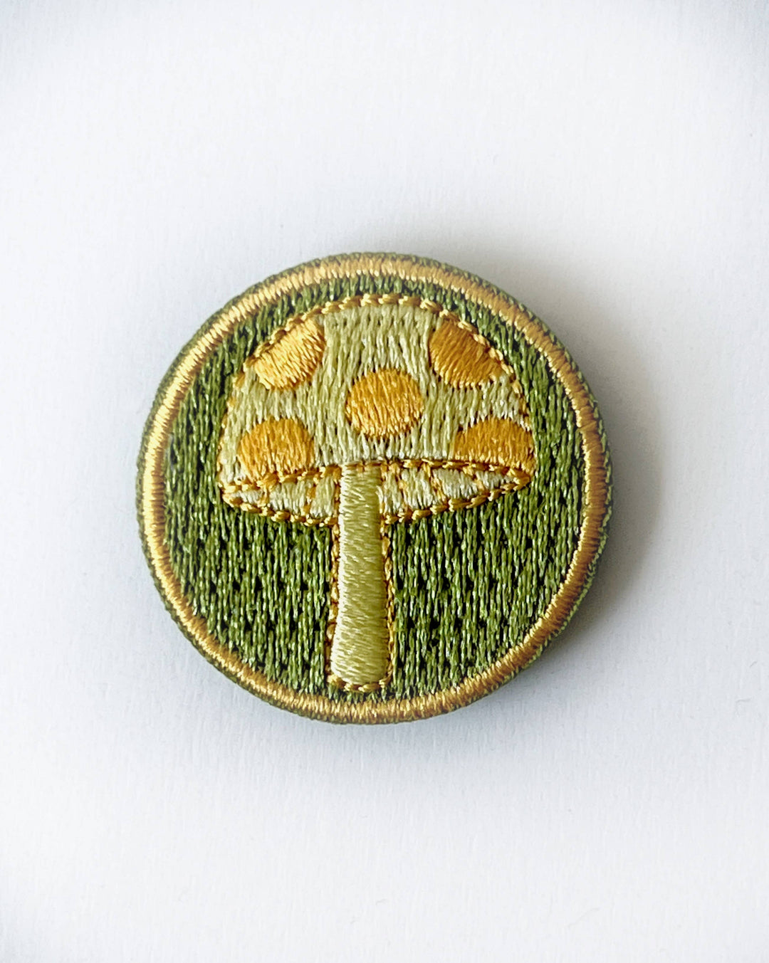 Rikrack embroidered mushroom needle minder featuring a golden yellow mushroom on a moss green background with a circular embroidered border.