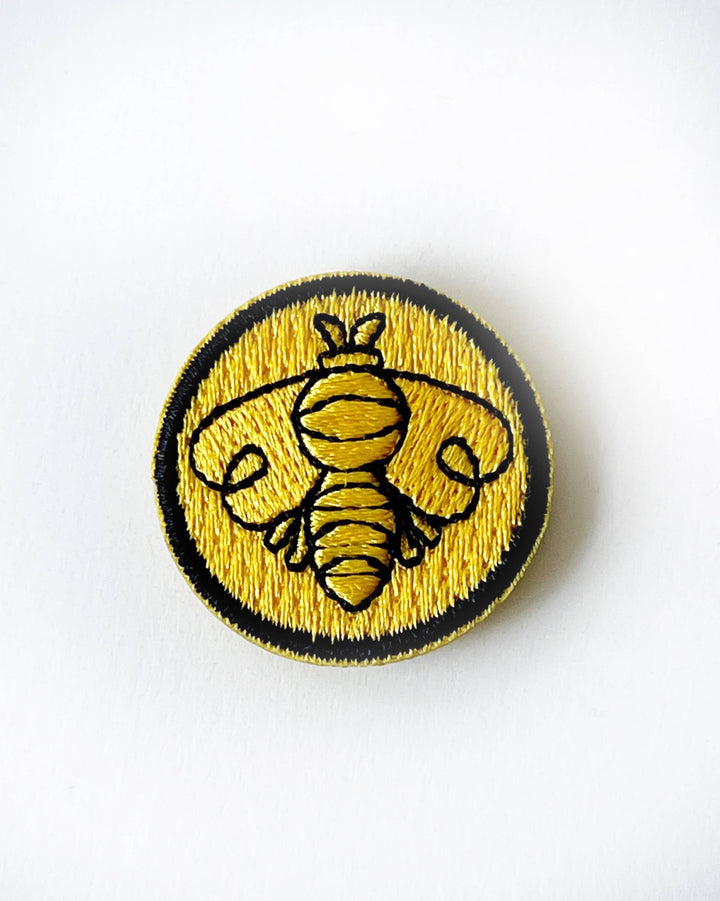 Rikrack embroidered bee needle minder featuring a black outlined honeybee on a golden yellow background with a circular black embroidered border.