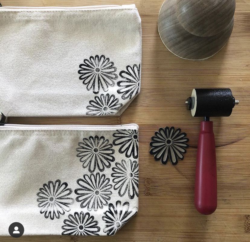Two fabric pouches with floral patterns, a wooden stamp, and a red-handled roller on a wooden surface.