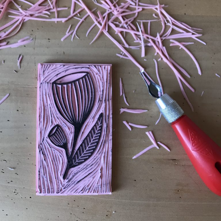 Pink rubber stamp with floral design and carving tool on a wooden surface